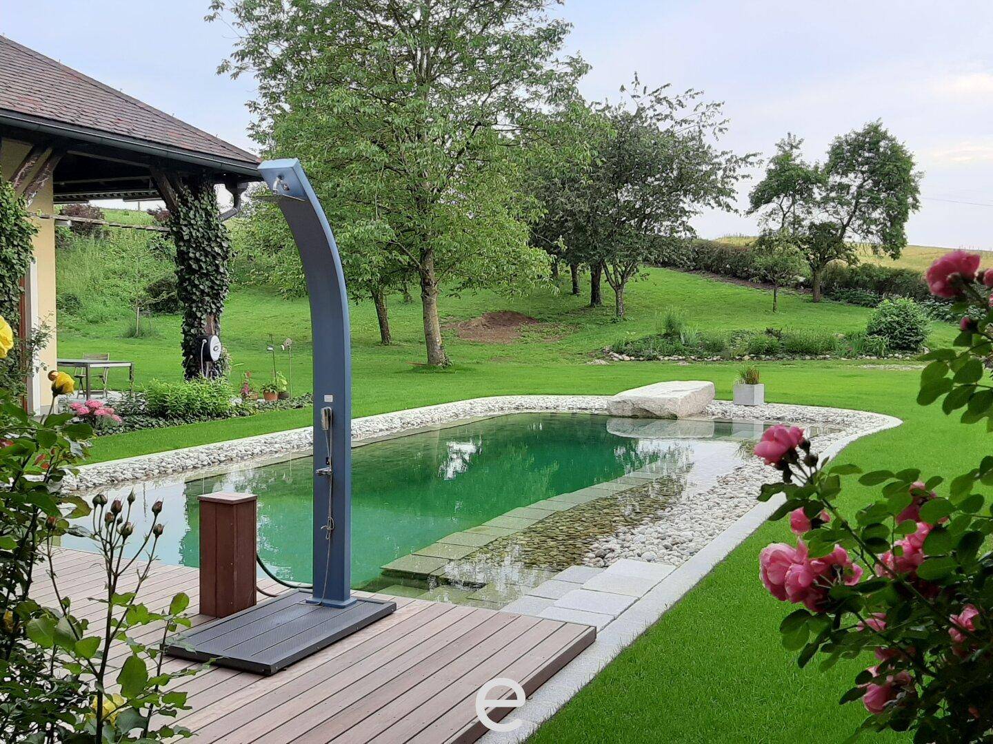 Poolbereich mit Holzdeck, Außendusche und blühenden Rosen im weitläufigen Garten.