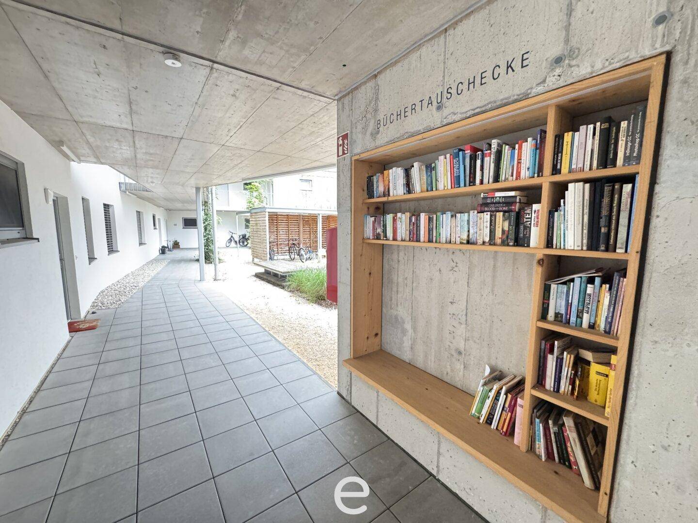 Überdachter Außenbereich mit Bücherregal zum Tauschen und Blick auf den Innenhof der Anlage.