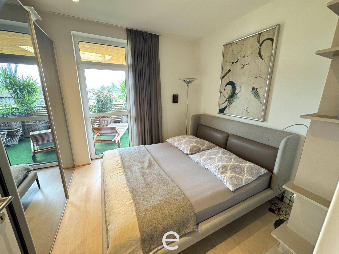 Helles Schlafzimmer mit Doppelbett, Holzboden und direktem Zugang zum sonnigen Balkon.