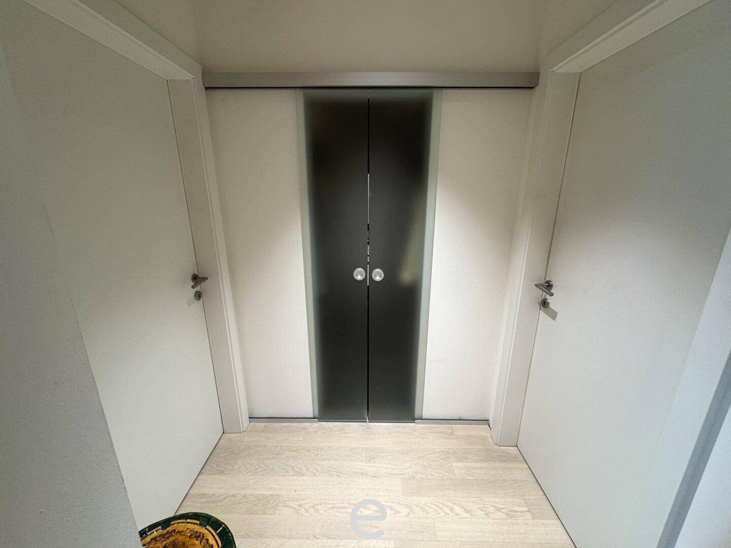 Heller Flur mit Holzboden und modernen Schiebetüren, die zu den angrenzenden Räumen führen.
