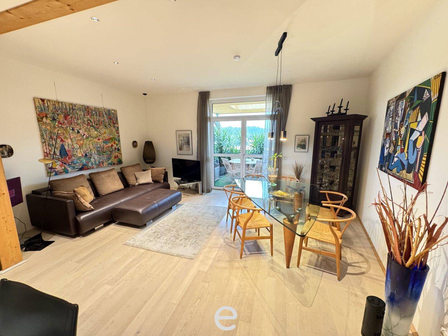 Geräumiger Wohn-Essbereich mit hellem Holzboden, bequemer Couch und Zugang zum Balkon.