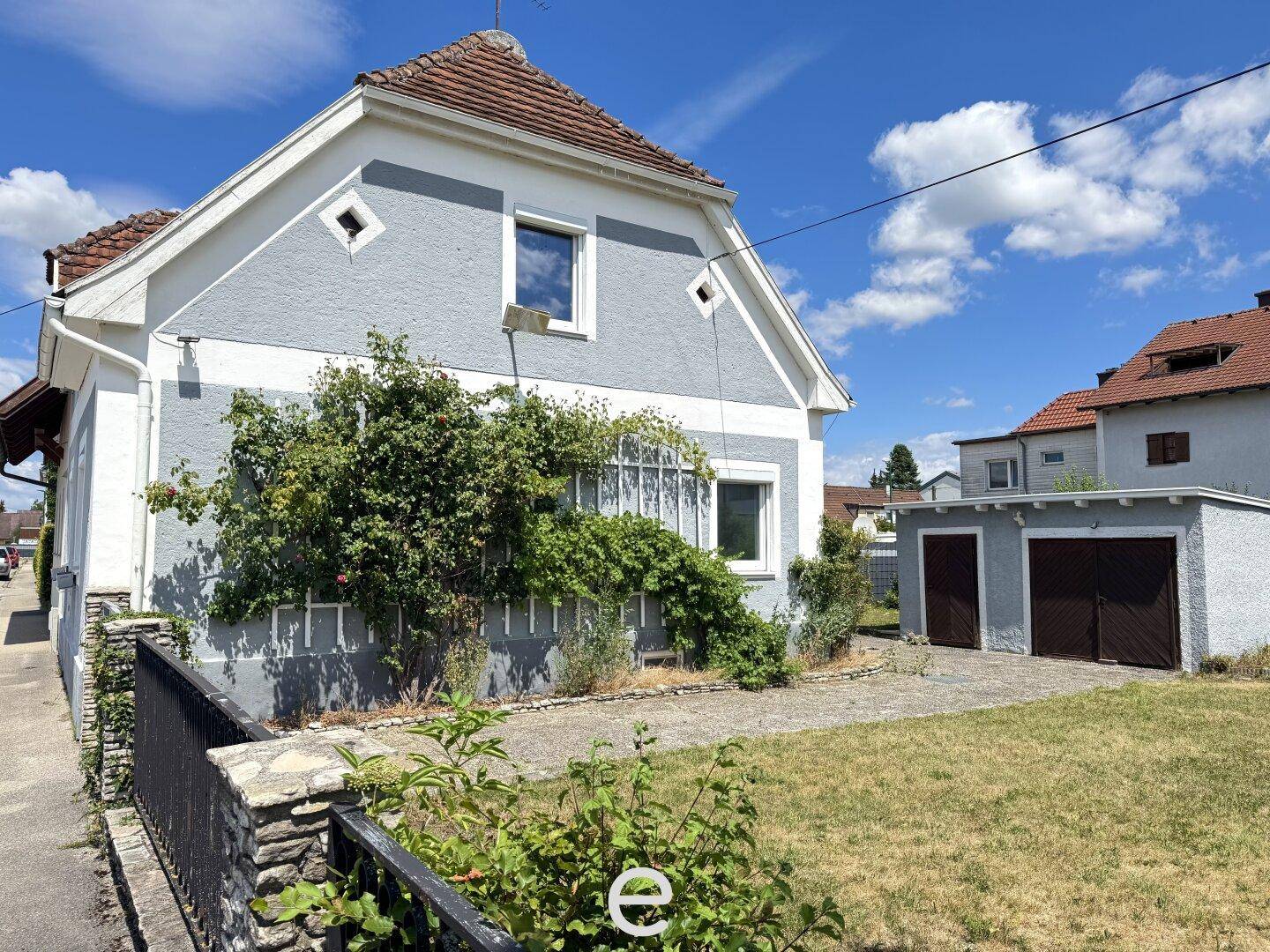 Ansicht des Einfamilienhauses mit Garage und Vorgarten unter einem sonnigen Himmel.