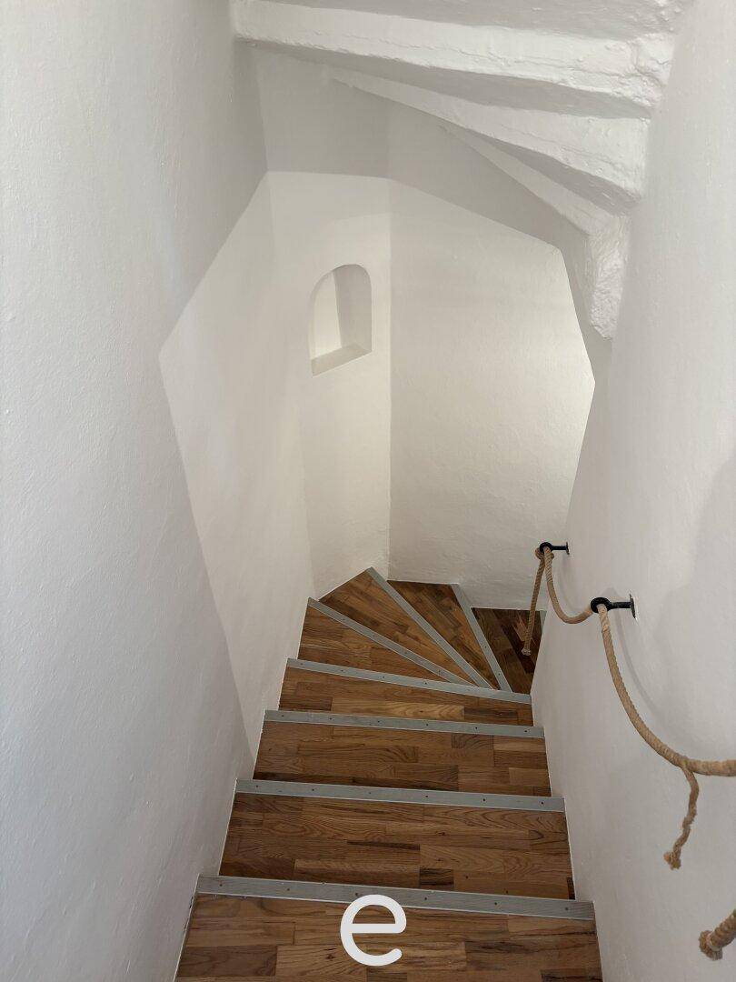 Wendeltreppe mit Holzstufen und einem Seilgeländer, die zu den oberen Etagen führt.
