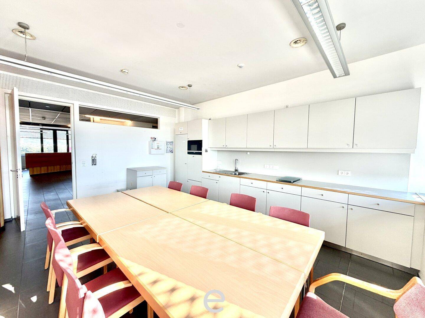 Großer Besprechungsraum mit langem Holztisch, Stühlen und weißen Einbauschränken entlang einer Wand.