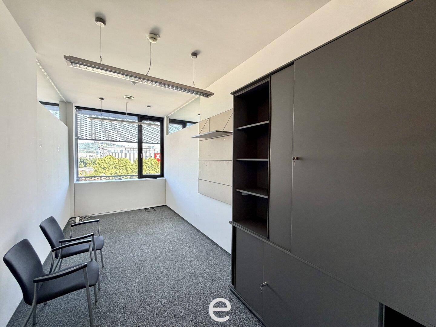 Kleiner Büroraum oder Wartebereich mit zwei Stühlen, großem grauen Schrank und Teppichboden.