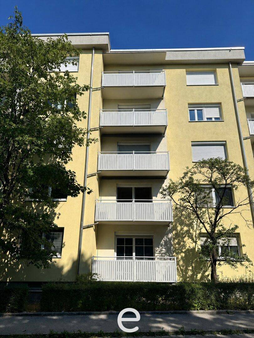 Mehrstöckiges Wohngebäude mit gelber Fassade und weißen Balkonen unter blauem Himmel.