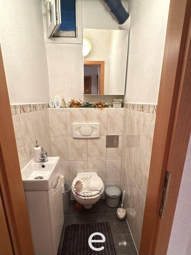 Kleines Gäste-WC mit wandhängendem WC, kompaktem Waschbecken und einem Fenster.