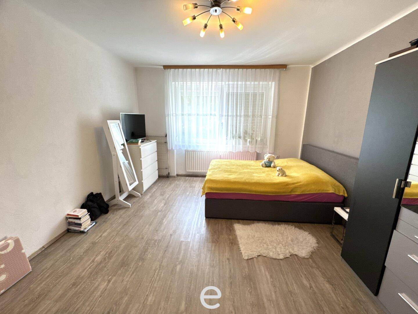 Helles Schlafzimmer mit Laminatboden, großem Fenster und einem modernen Bett mit gelber Decke.