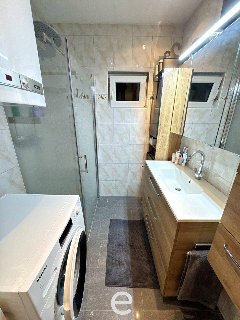 Modernes Badezimmer mit Dusche, Waschbecken, Waschmaschine und einem kleinen Fenster.
