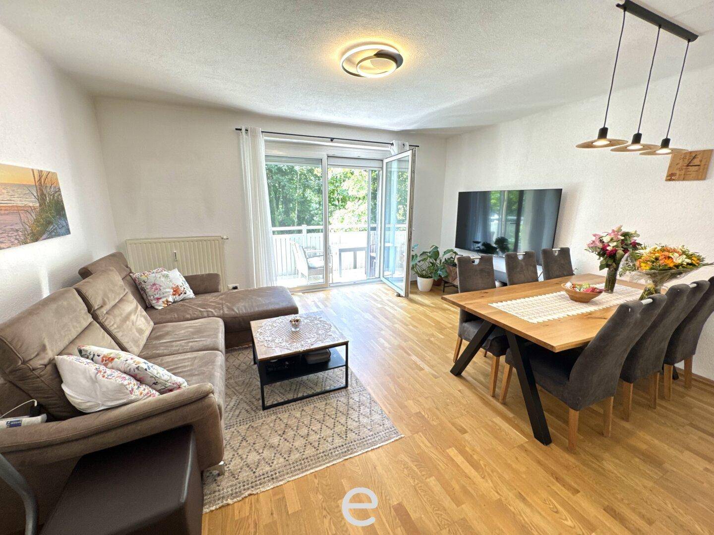 Geräumiger Wohn-Essbereich mit Holzboden, großem Esstisch und direktem Zugang zum Balkon.