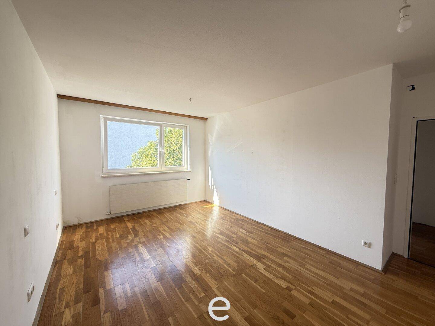 Helles Schlafzimmer mit Parkettboden und Fenster mit Blick ins Grüne.