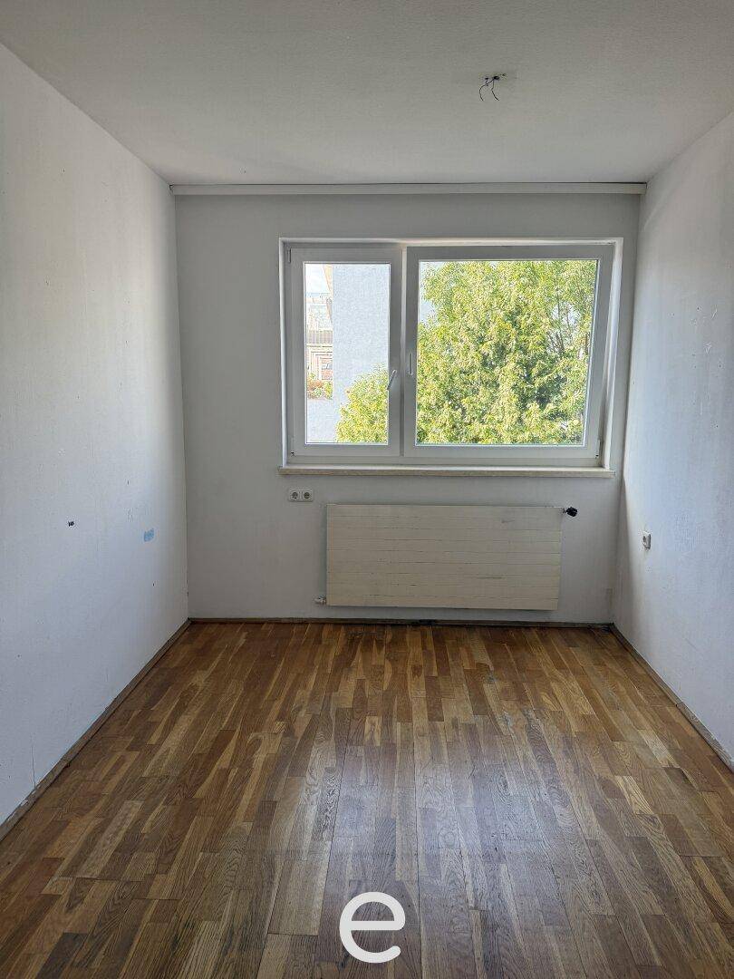 Kleineres Schlafzimmer mit Holzboden und Fenster mit Blick auf Bäume.