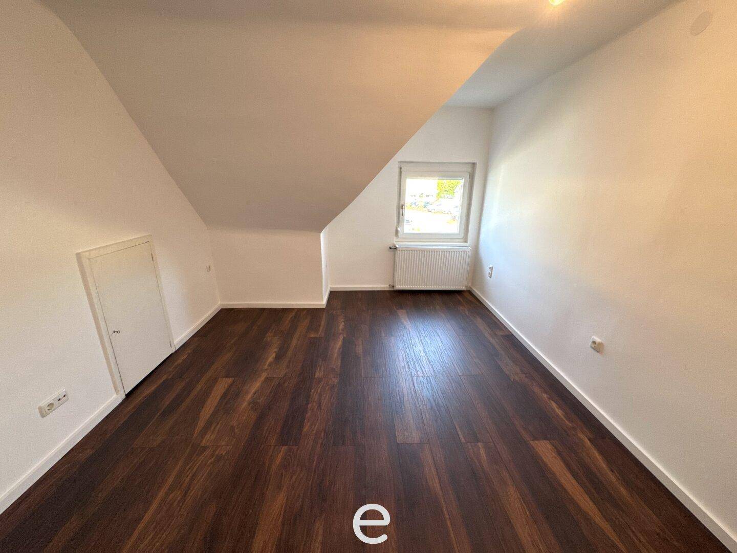 Geräumiges Dachzimmer mit dunklem Laminatboden, Fenster und charakteristischer Dachschräge.