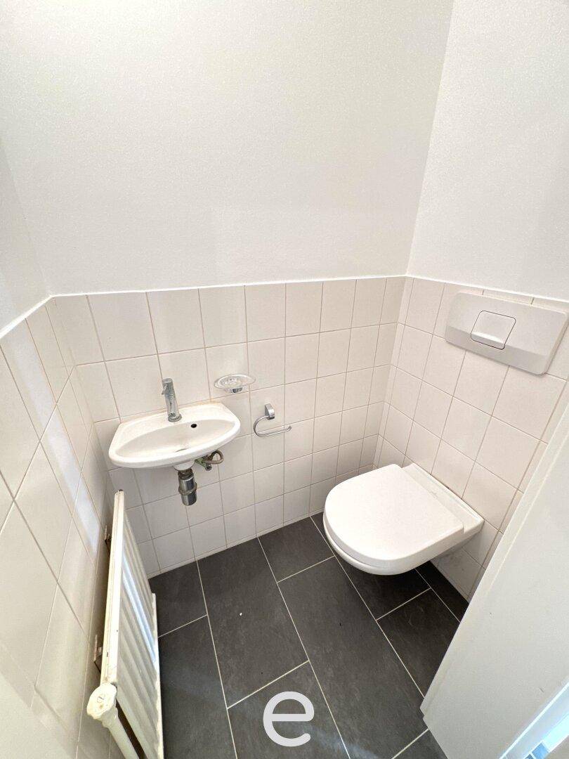 Kleines Gäste-WC mit wandhängender Toilette, kleinem Waschbecken und dunklem Fliesenboden.