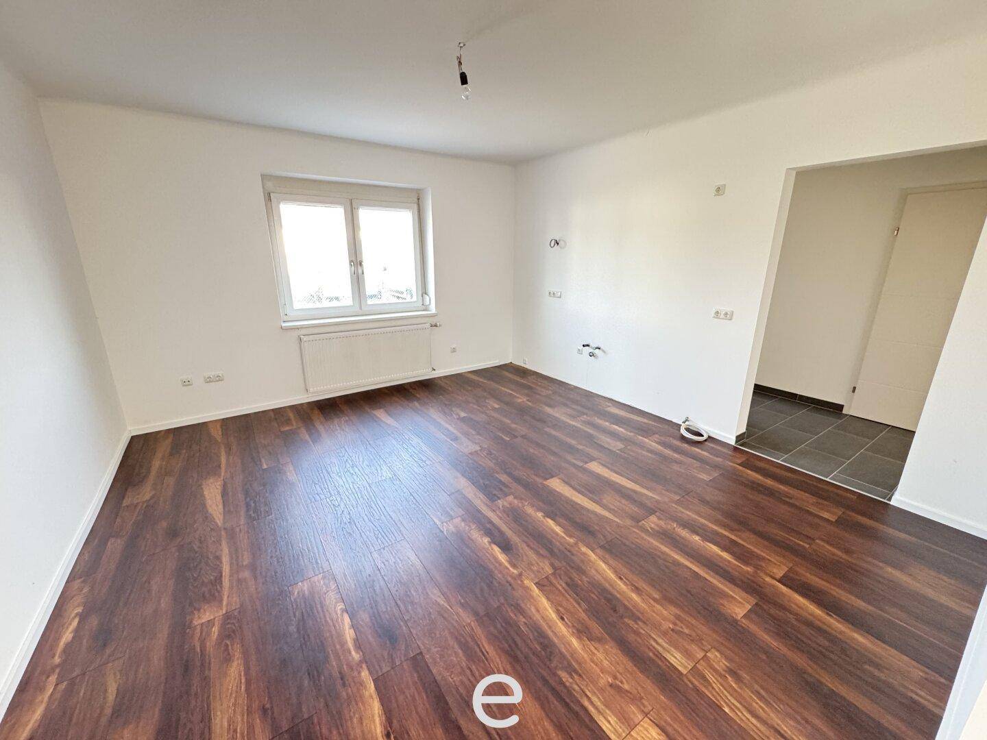 Geräumiges Zimmer mit dunklem Laminatboden und einem Fenster, das viel Tageslicht hereinlässt.
