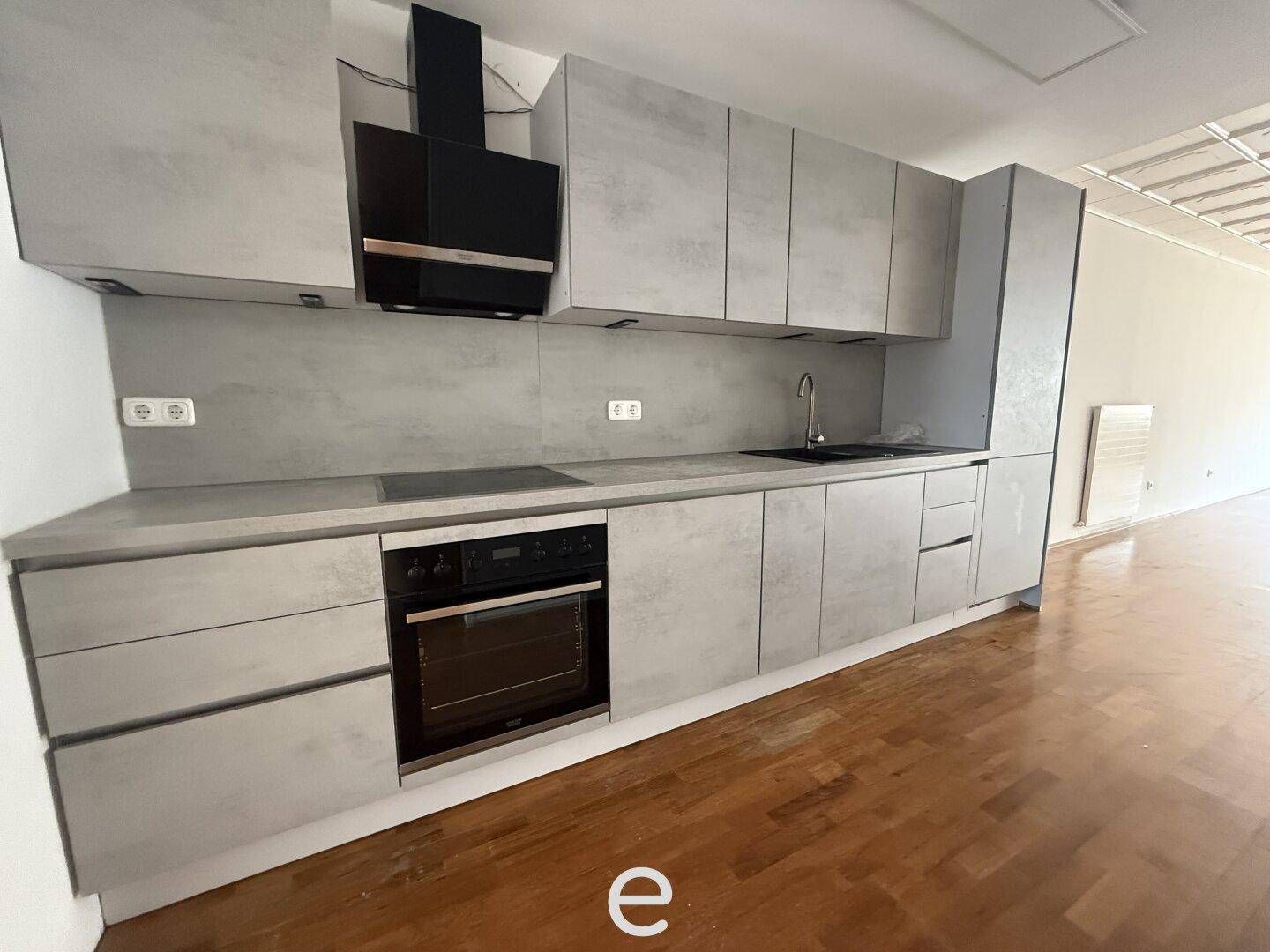 Moderne Einbauküche in Grau mit integriertem Backofen und Dunstabzugshaube.