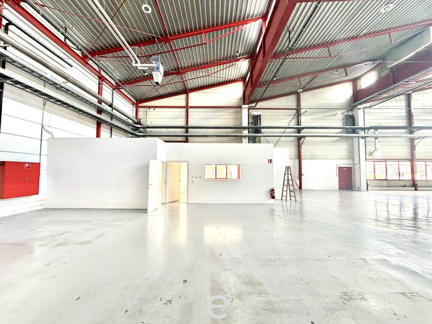Weitläufige Lagerhalle mit Betonboden, hohen Decken und einem abgetrennten Bereich für Büros.