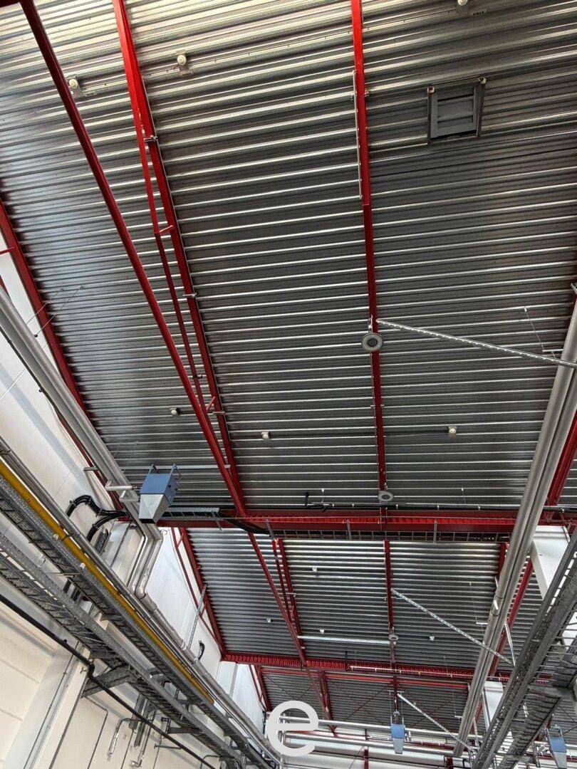 Detaillierte Ansicht der Deckenkonstruktion einer Industriehalle mit Lüftungsrohren und Beleuchtung.