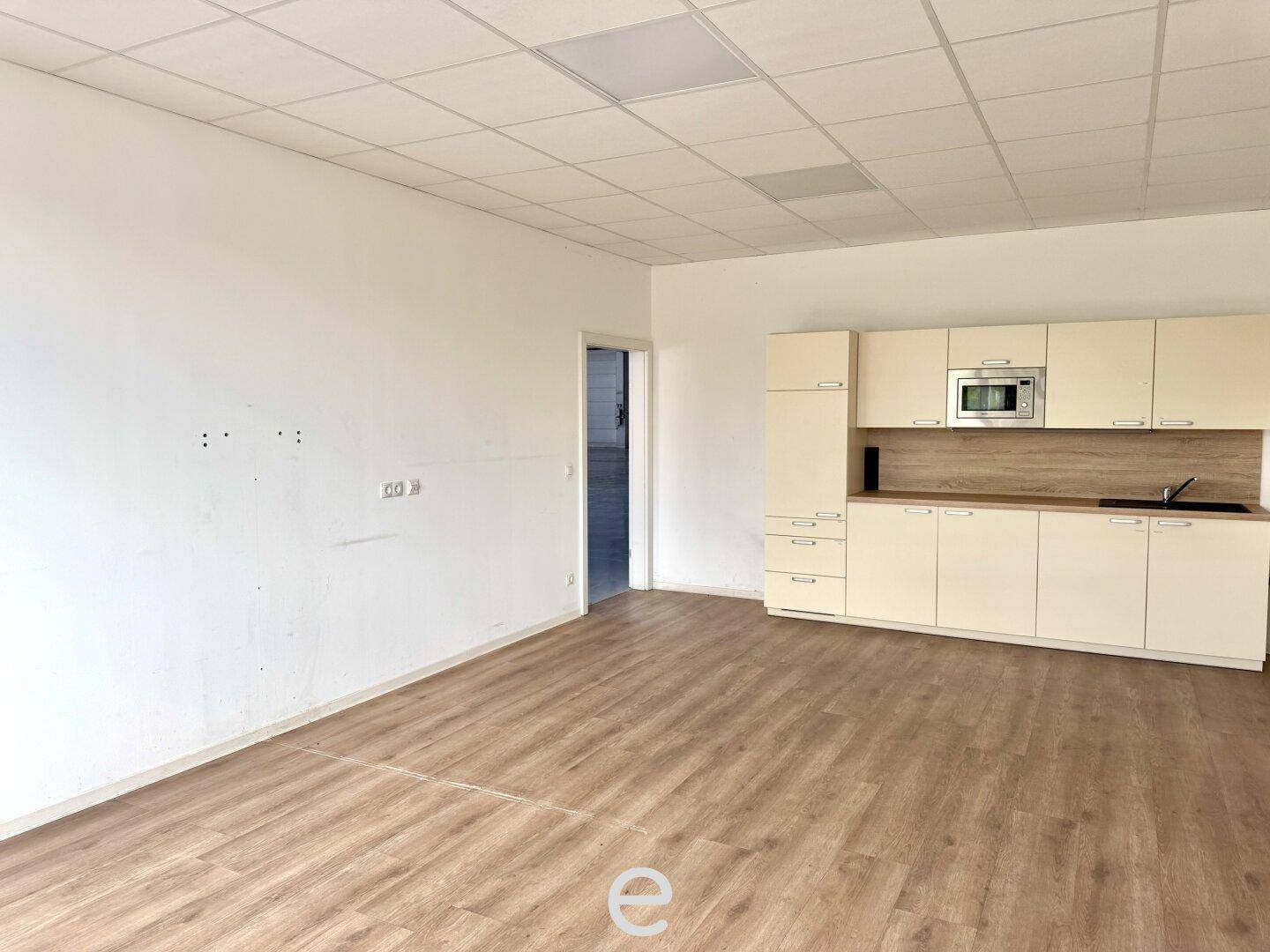 Kleiner Büroraum mit integrierter Küchenzeile, Laminatboden und abgehängter Decke.