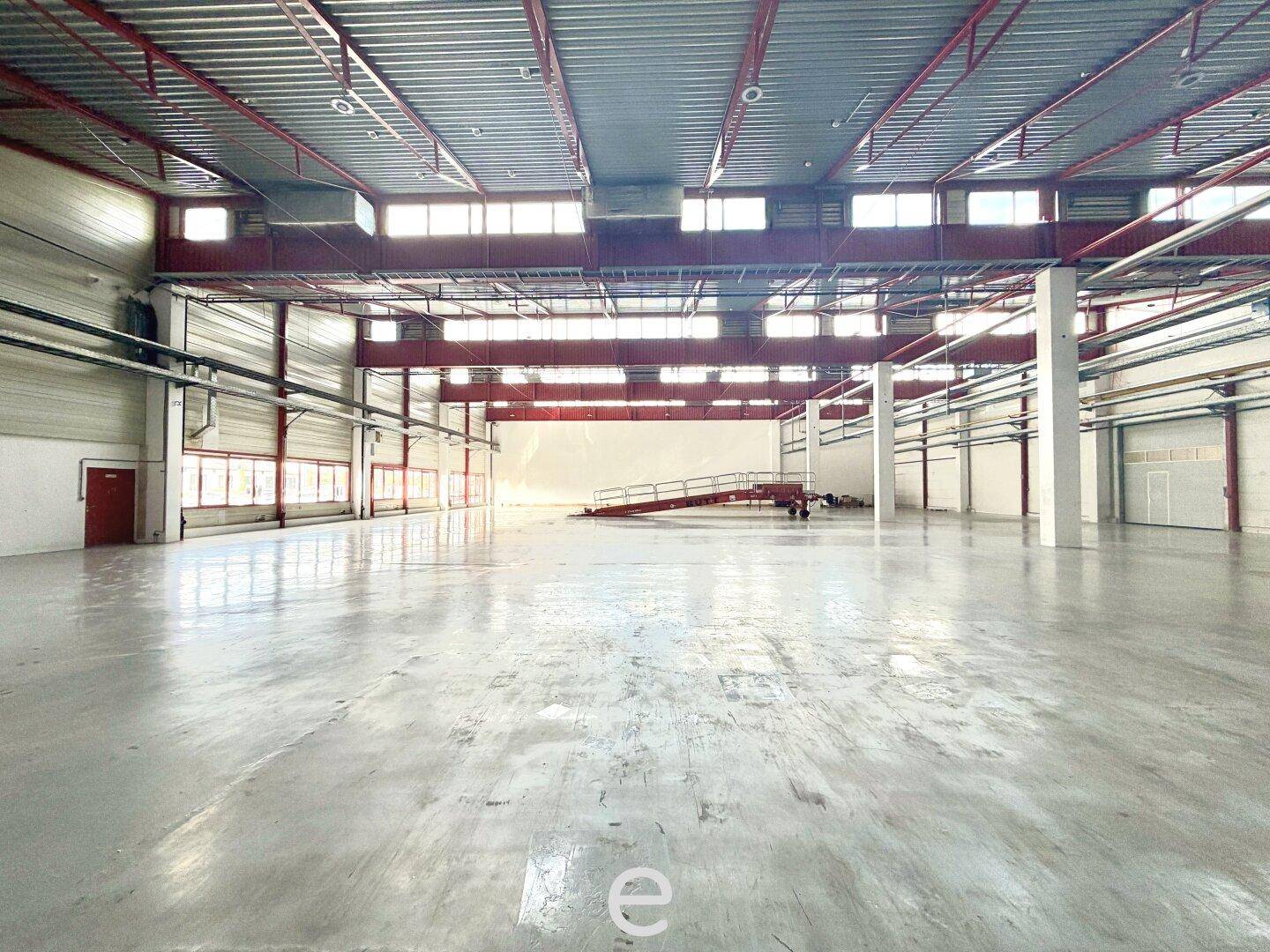 Große, helle Lagerhalle mit Betonboden, hohen Decken und einer Laderampe im Hintergrund.
