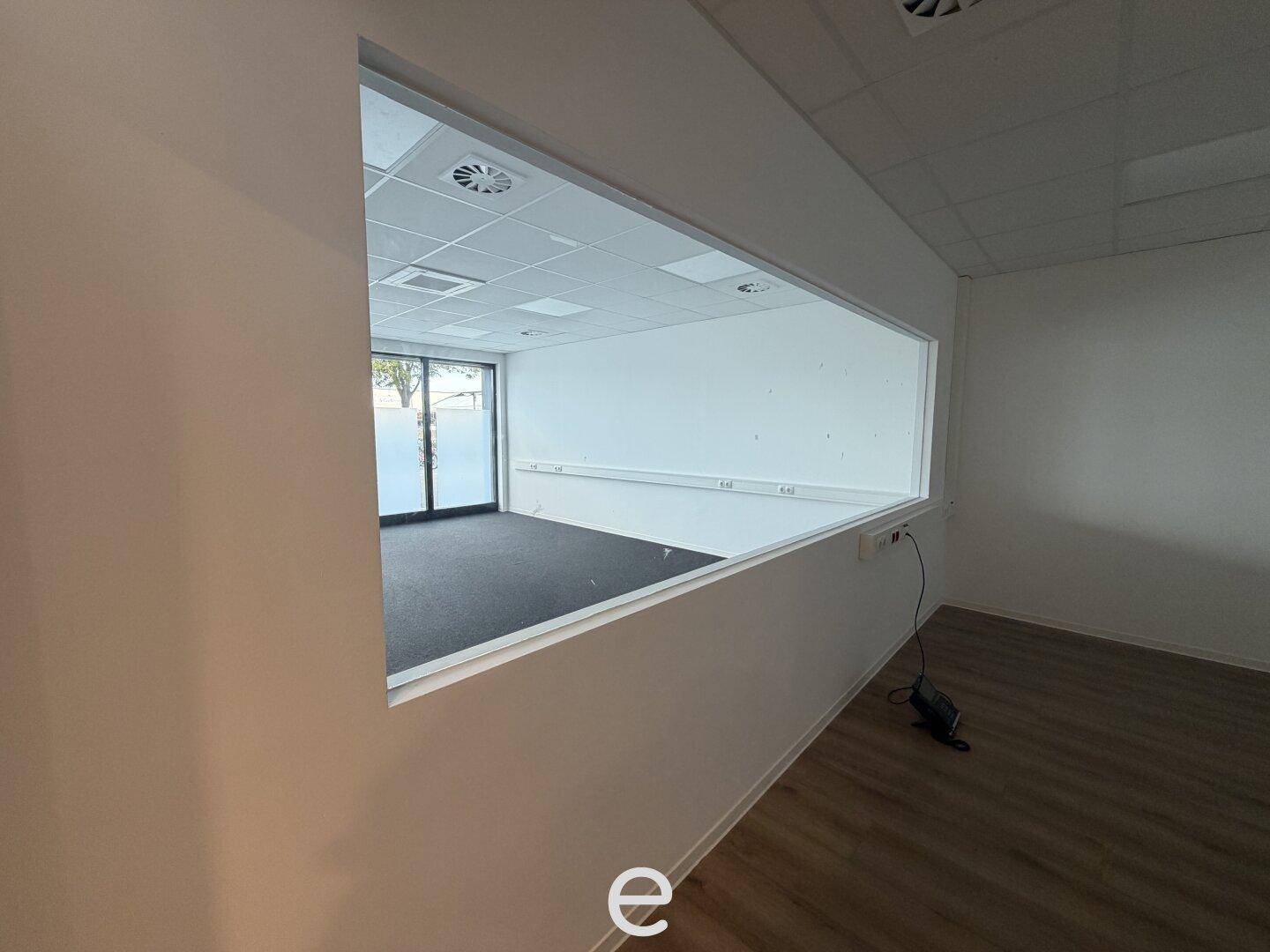 Blick durch eine interne Fensteröffnung in einen angrenzenden Büroraum mit Teppichboden und Fenstern.