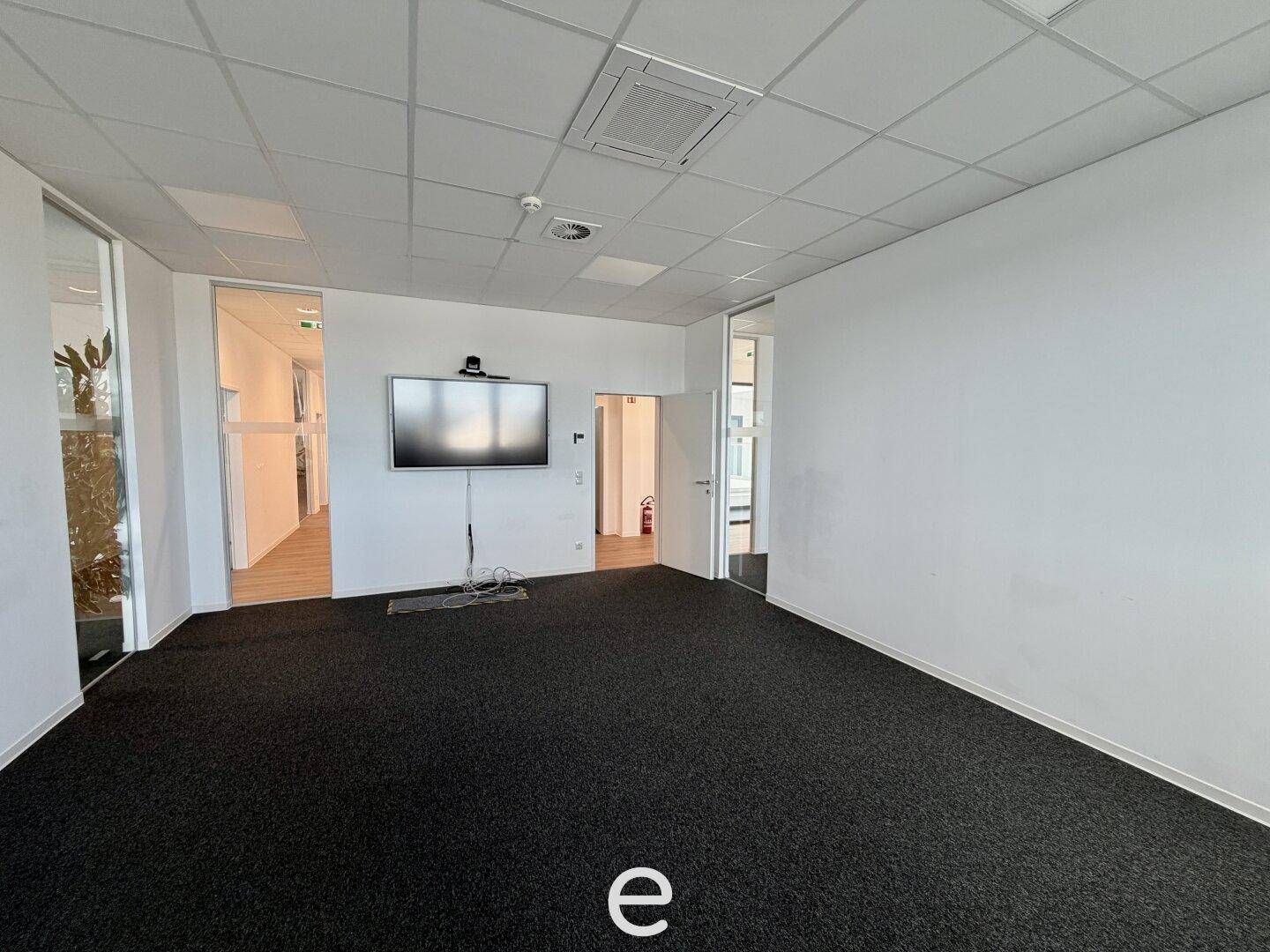 Büroraum mit Teppichboden und einem an der Wand montierten Bildschirm, ideal für Präsentationen.