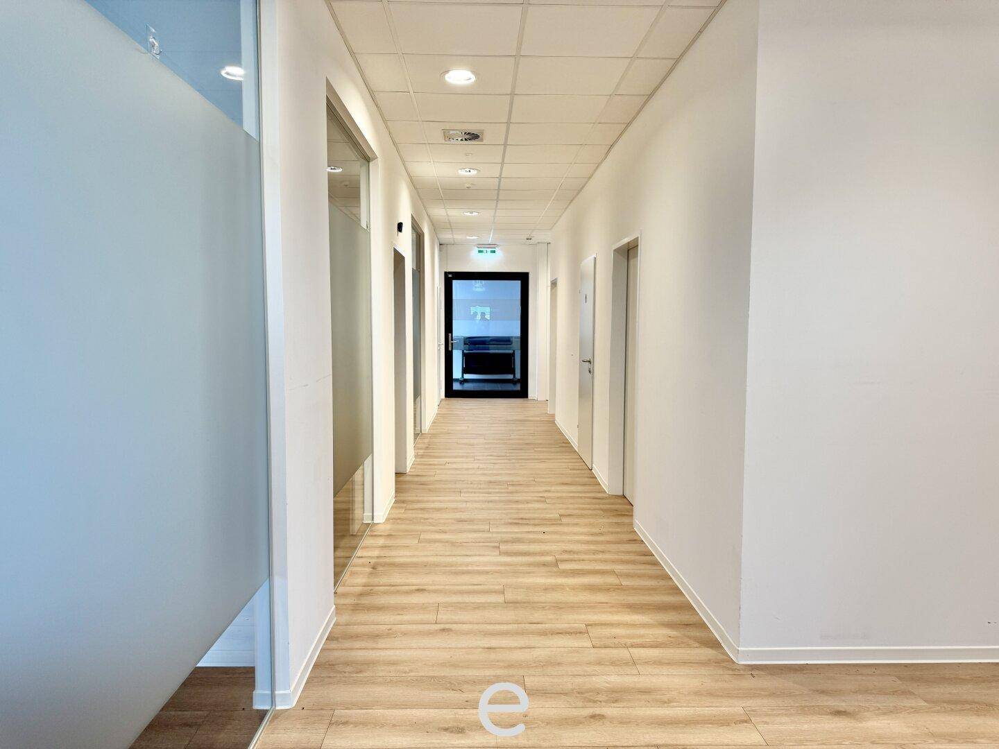 Langer, heller Bürogang mit Holzboden und Türen zu verschiedenen Büroräumen.
