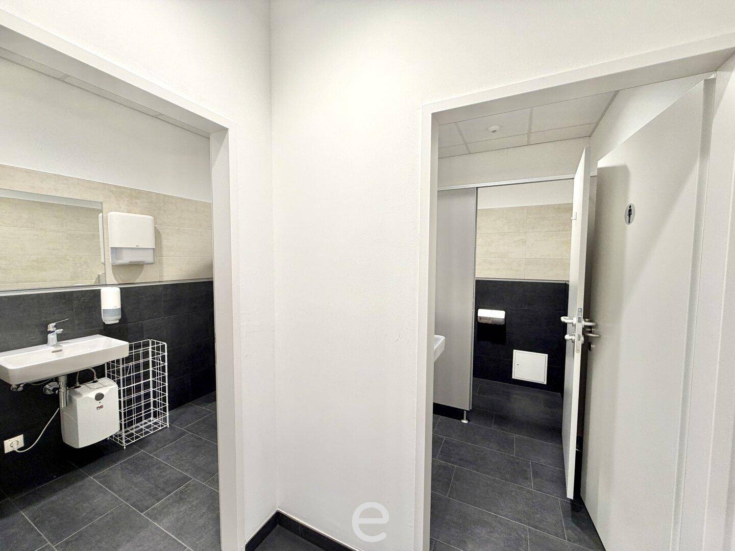 Moderne Toilettenräume mit dunklen Fliesen und weißen Waschbecken, sauber und funktional.