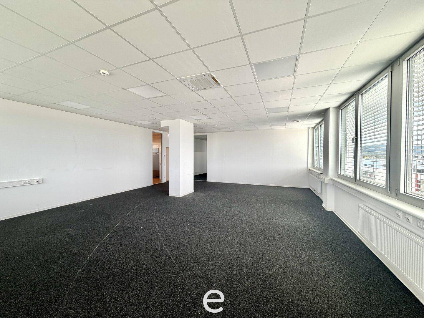 Helles und offenes Büro mit dunklem Teppichboden, weißen Wänden und einer Säule in der Mitte des Raumes.