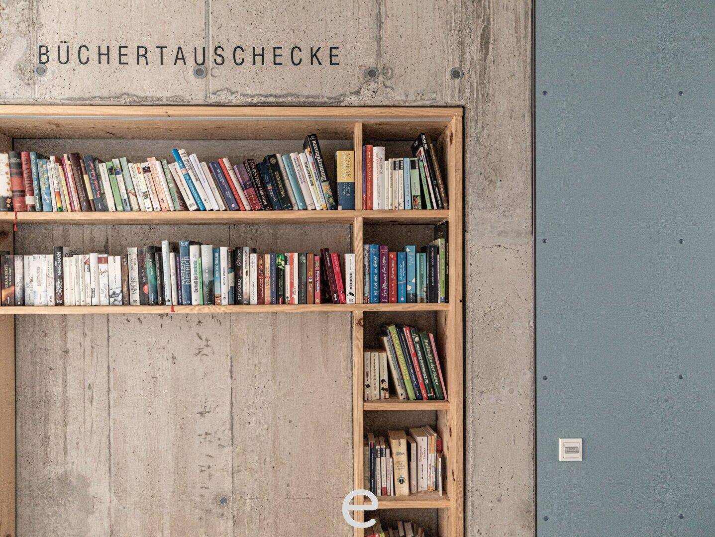 Eine eingebaute Bücherregalwand aus Holz in einer Betonwand, als Büchertauschecke genutzt.