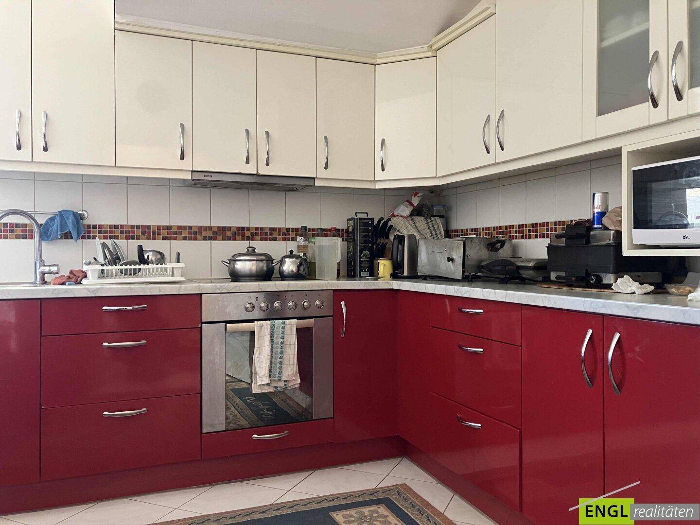 Funktionale Küche mit roten Unterschränken, weißen Oberschränken und Fliesen.