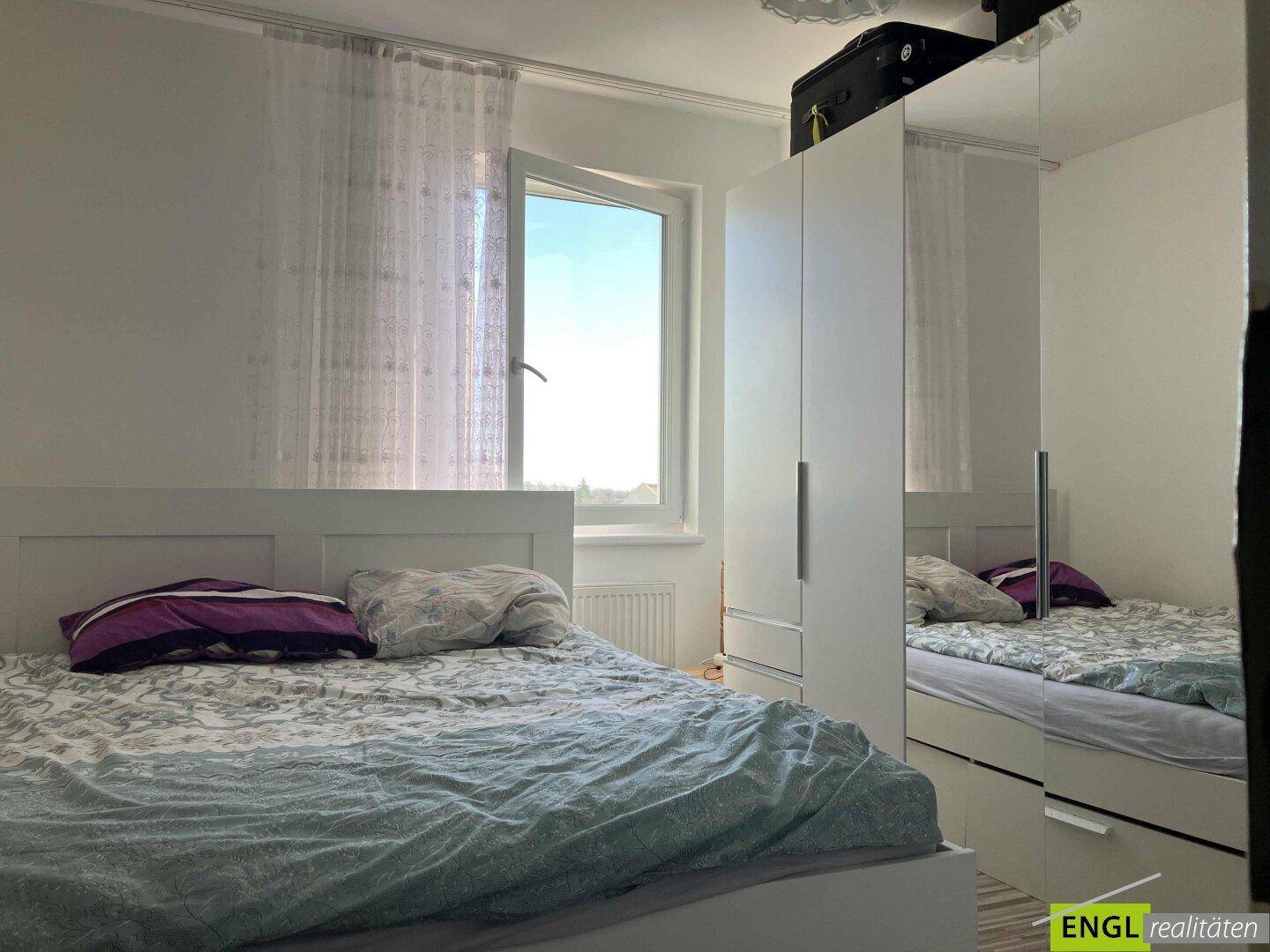 Helles Schlafzimmer mit Doppelbett, Kleiderschrank und Fenster.