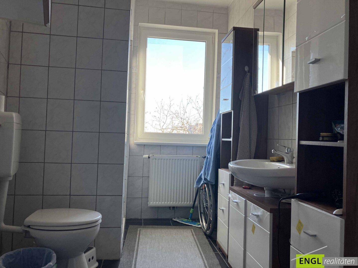 Gefliestes Badezimmer mit Fenster, Toilette und Waschbeckenunterschrank.