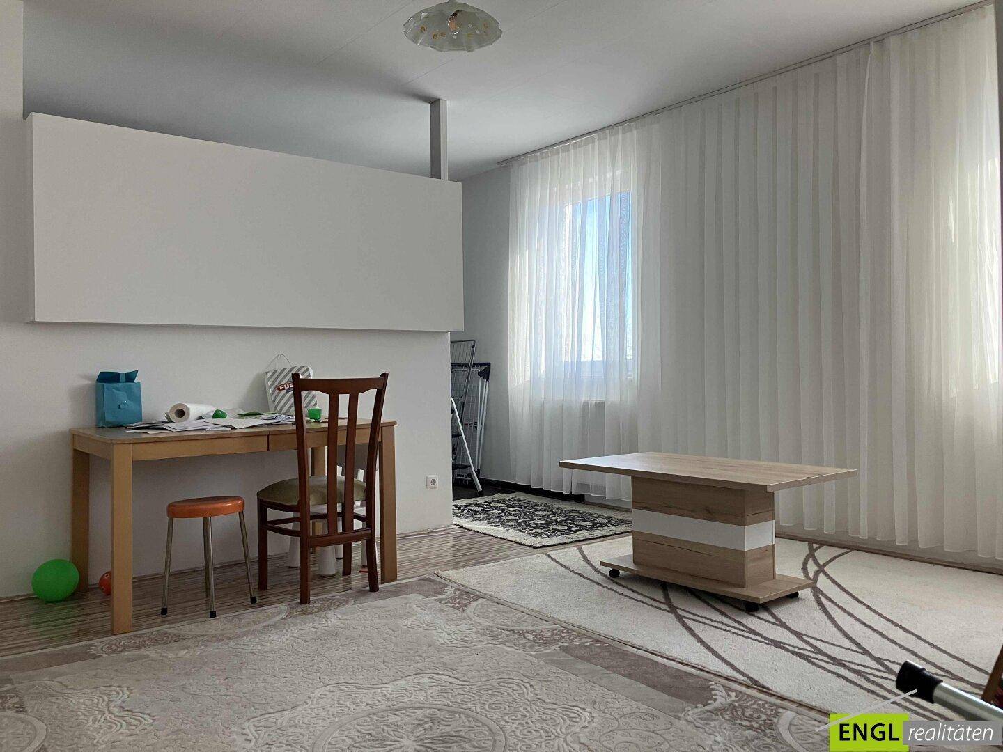 Heller Wohnbereich mit Schreibtisch, Couchtisch und großen Fenstern.