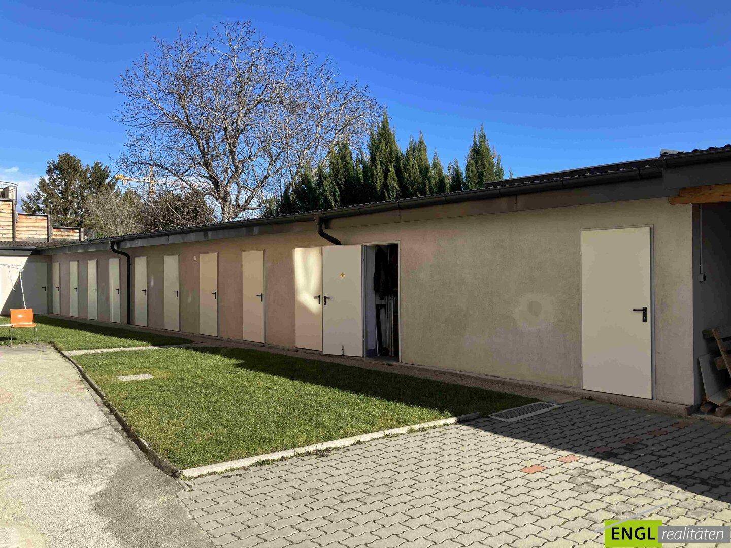 Reihe von Garagen und Abstellräumen mit gepflastertem Vorplatz und Rasenfläche.