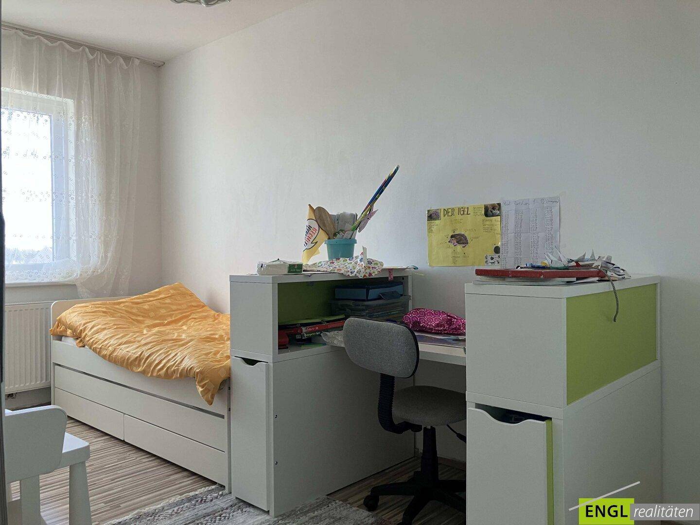 Helles Schlafzimmer mit Einzelbett, Schreibtisch und Fenster.