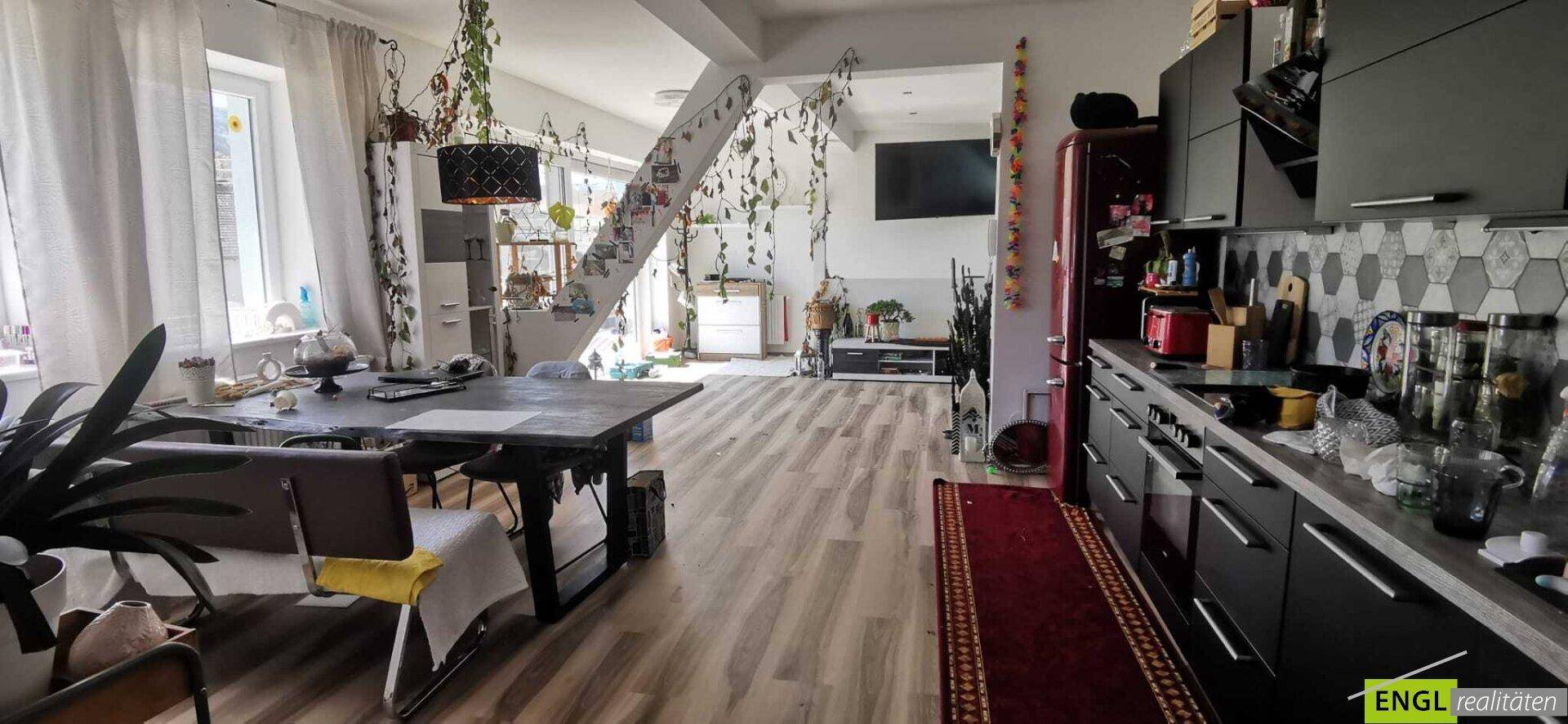 Geräumiger Wohn-Essbereich mit dunkler Küche, Esstisch und Treppe zum Obergeschoss.