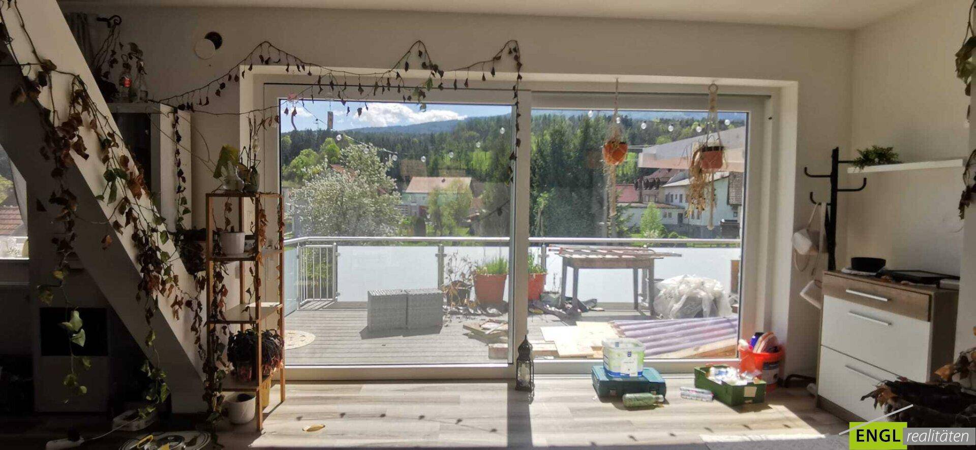 Wohnraum mit großem Fenster und Zugang zu einem Balkon mit Blick auf die Umgebung.