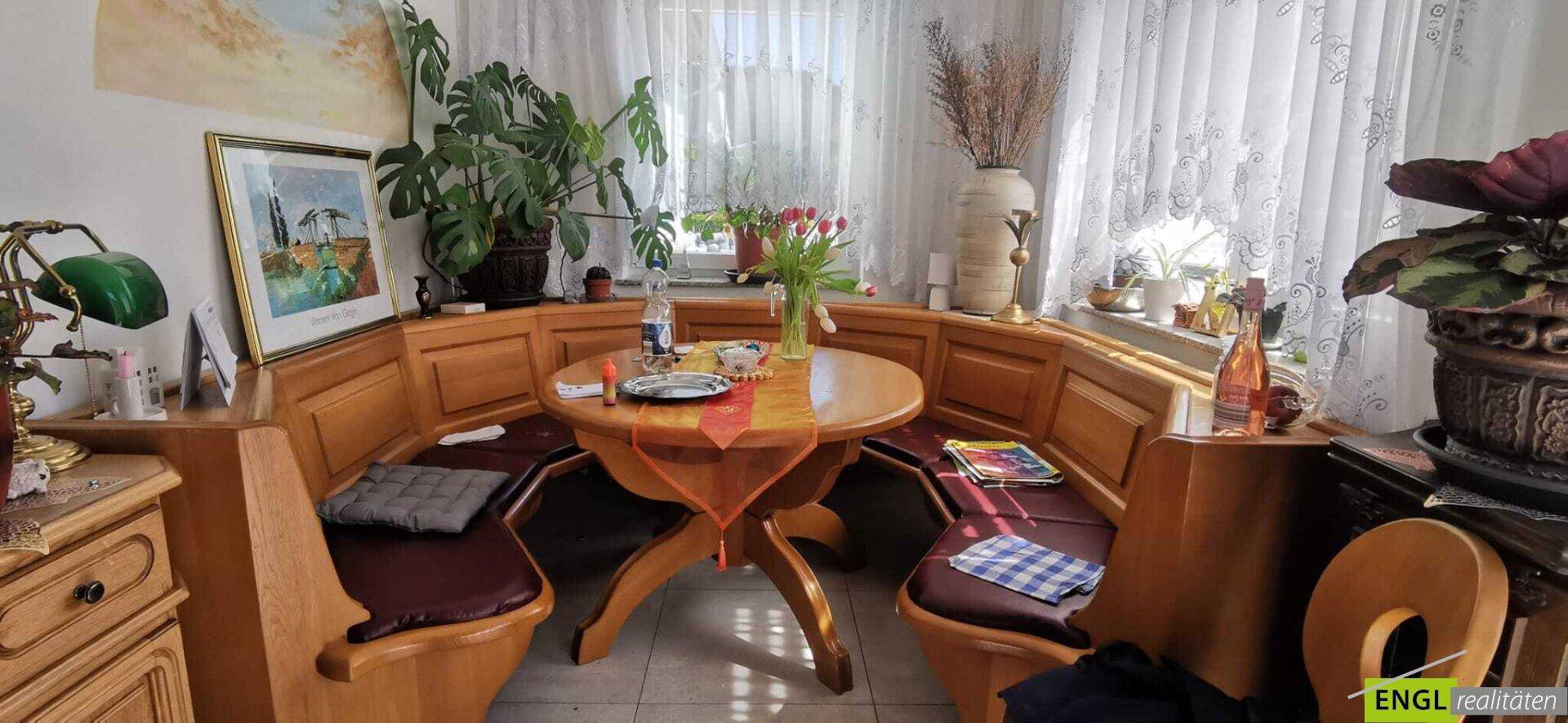 Gemütliche Essecke mit traditioneller Holzbank und Tisch, umgeben von Fenstern.