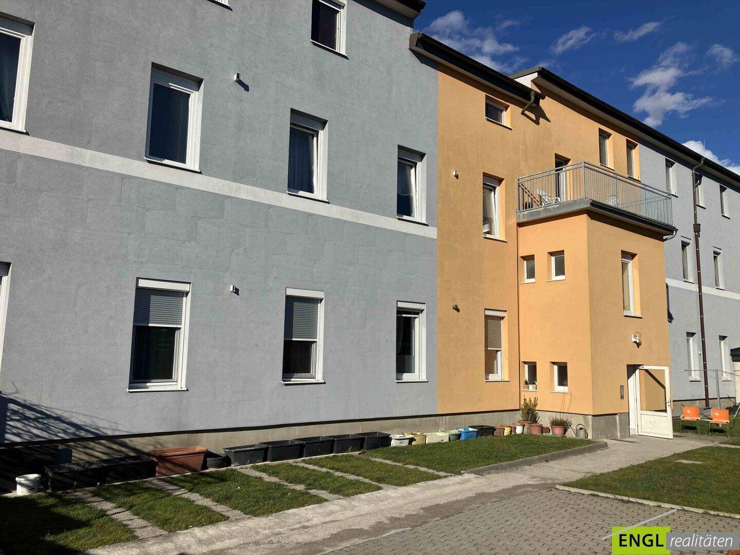 Seitenansicht des Gebäudes mit Balkon und kleinen Grünflächen im Erdgeschoss.