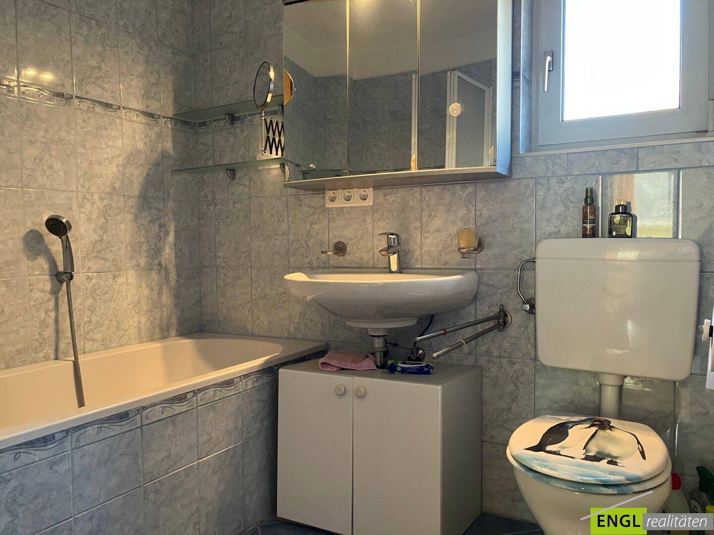 Badezimmer mit blauen Fliesen, Badewanne, Waschbecken und WC, ausgestattet mit einem Spiegelschrank.