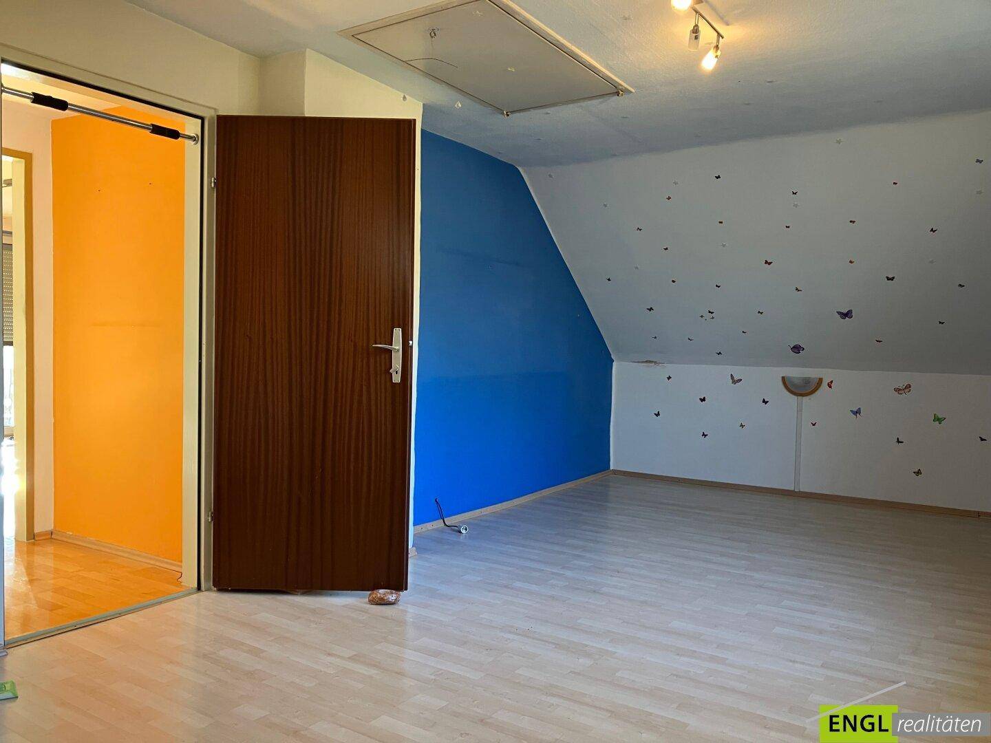 Dachgeschosszimmer mit Laminatboden, einer farbenfrohen Wandgestaltung und schräger Decke.