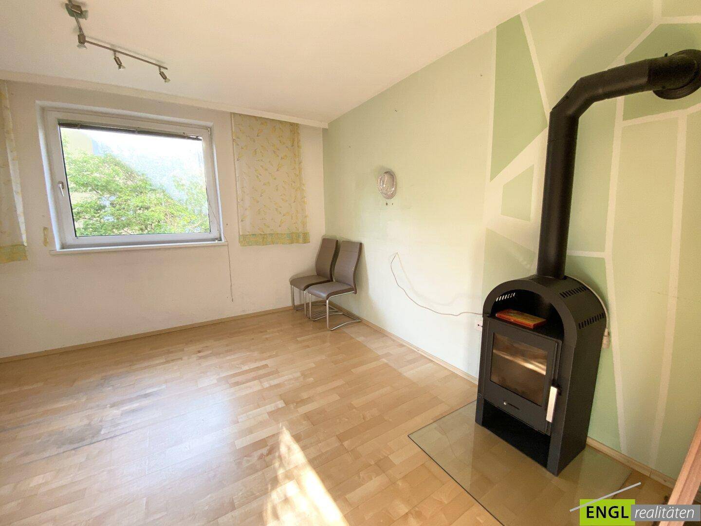 Helles Wohnzimmer mit Holzboden, einem modernen Holzofen und einer farblich abgesetzten Wand.