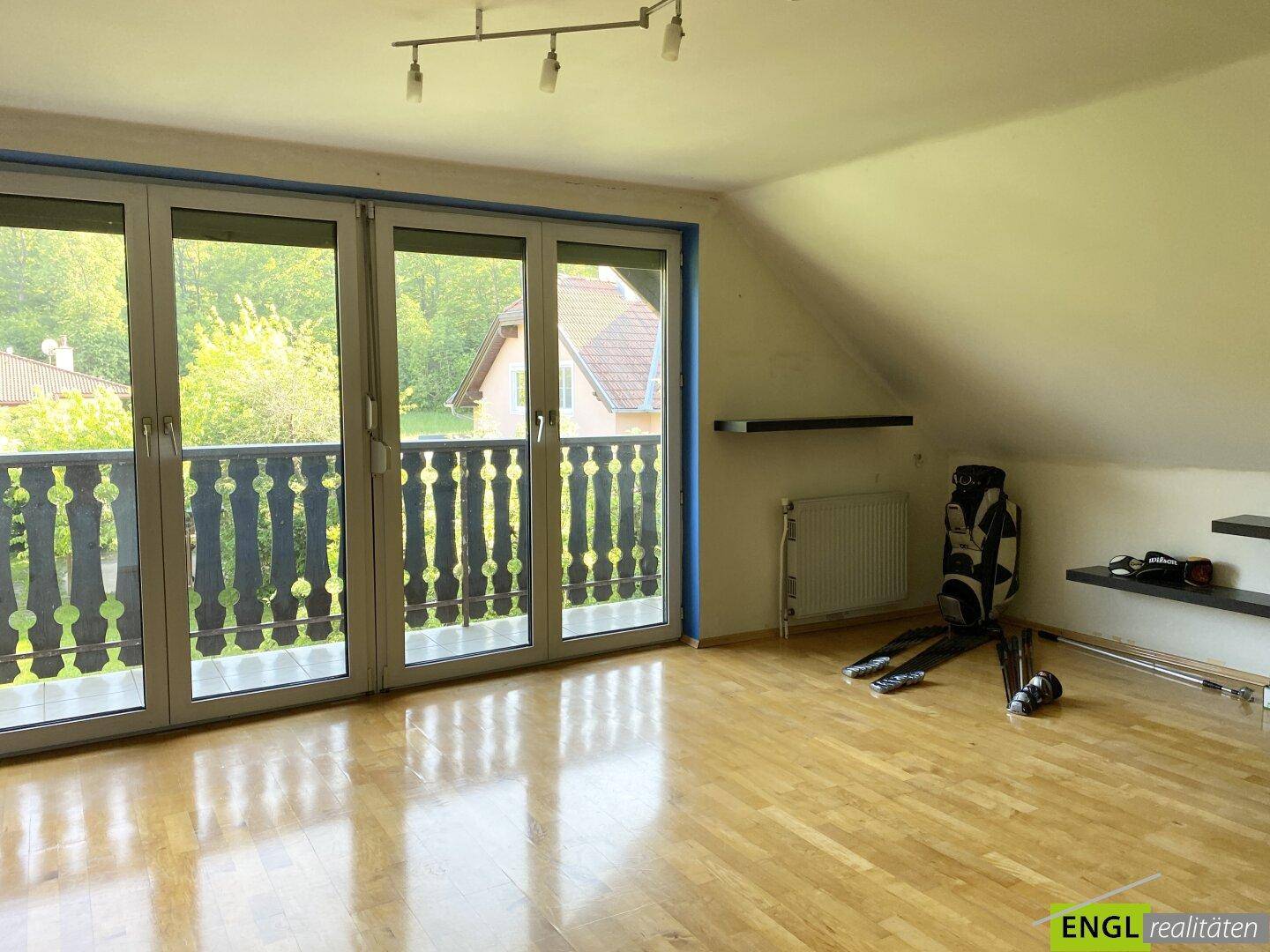 Geräumiges Zimmer im Dachgeschoss mit Holzboden, Zugang zu einem Balkon und schrägen Decken.