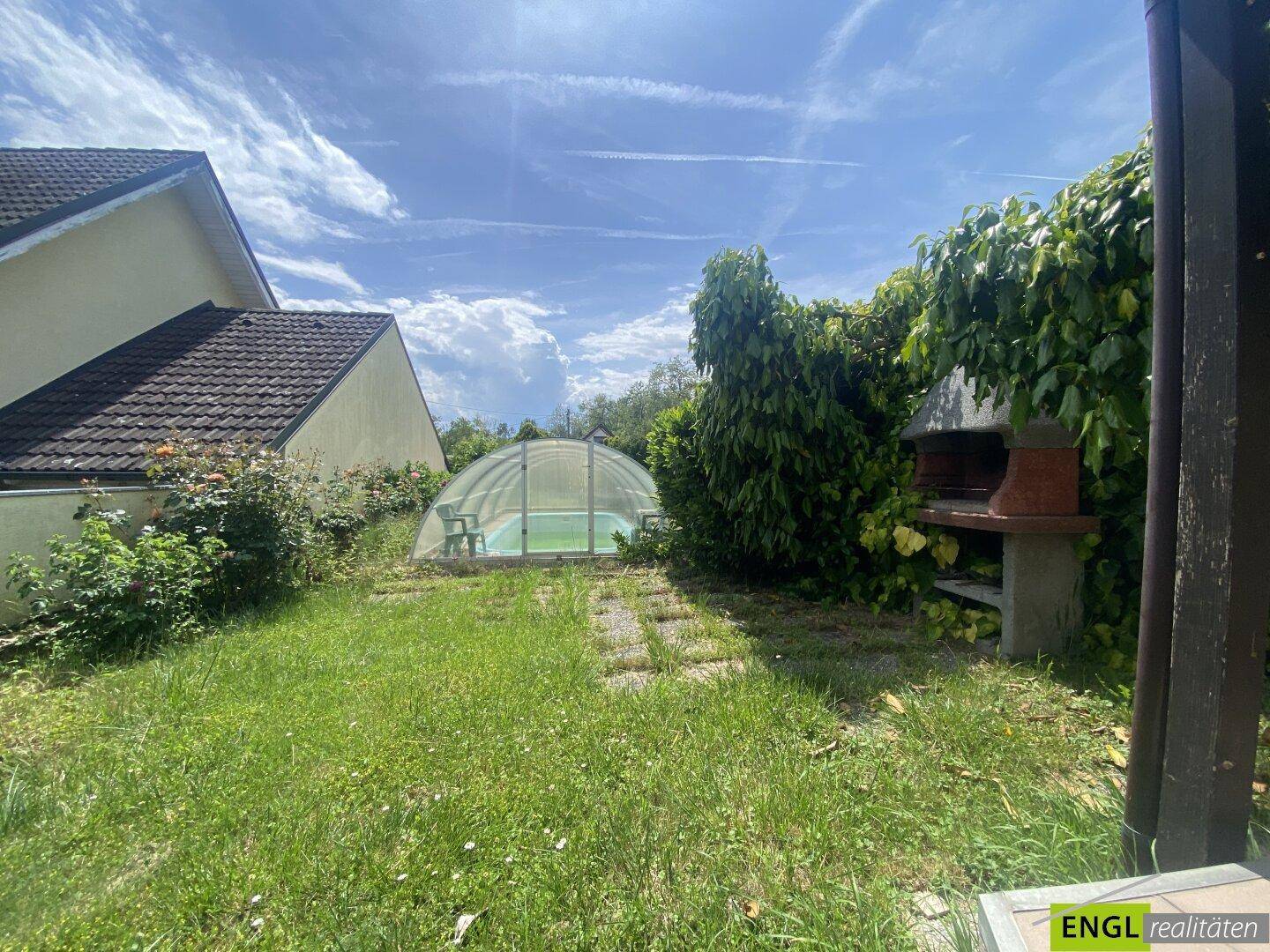 Sonniger Garten mit Rasenfläche, überdachtem Pool und gemauertem Grill für entspannte Stunden.