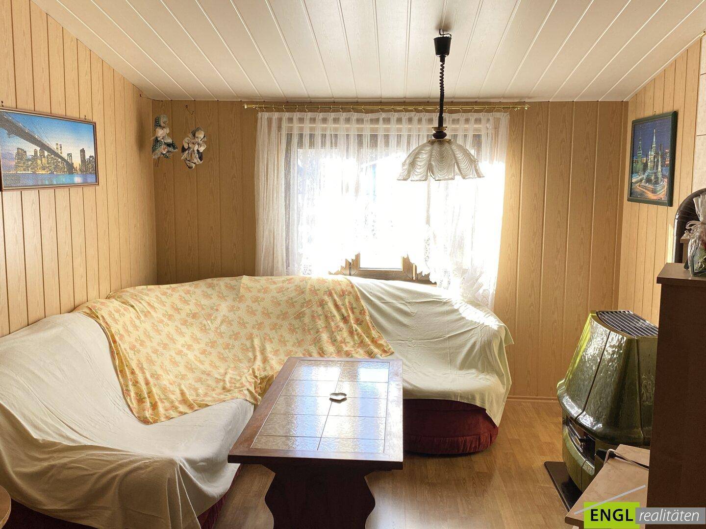 Gemütliches Wohnzimmer mit Holzvertäfelung, Kaminofen und Blick in den Garten.