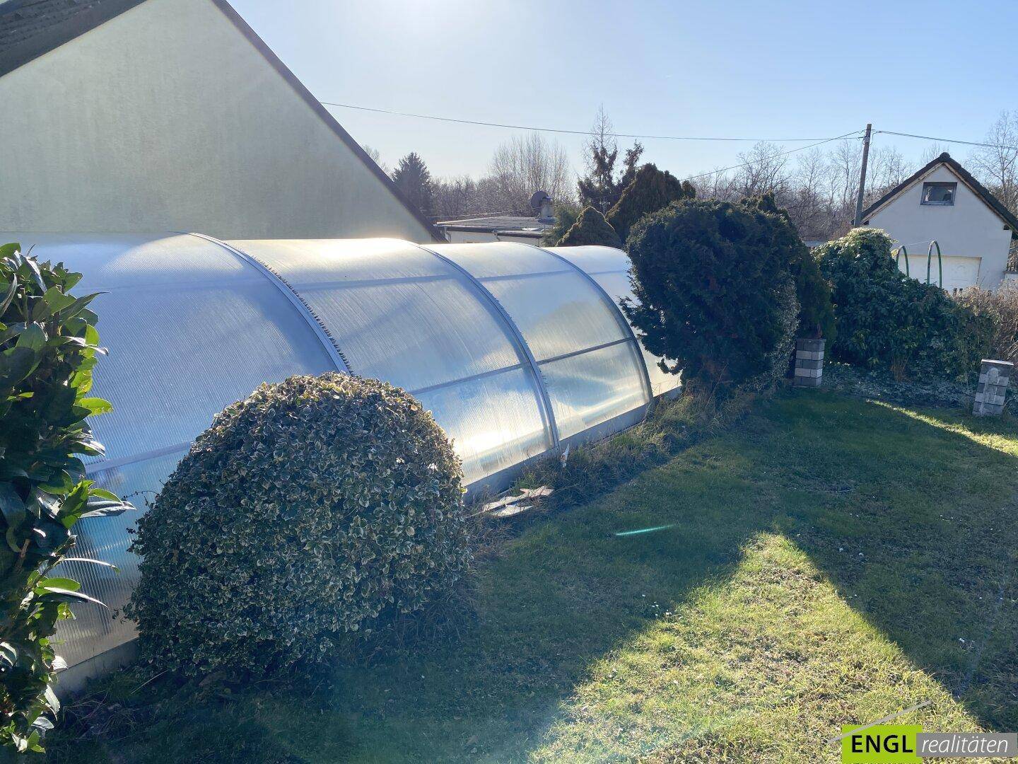 Detailansicht des überdachten Swimmingpools im Garten, umgeben von gepflegten Büschen.