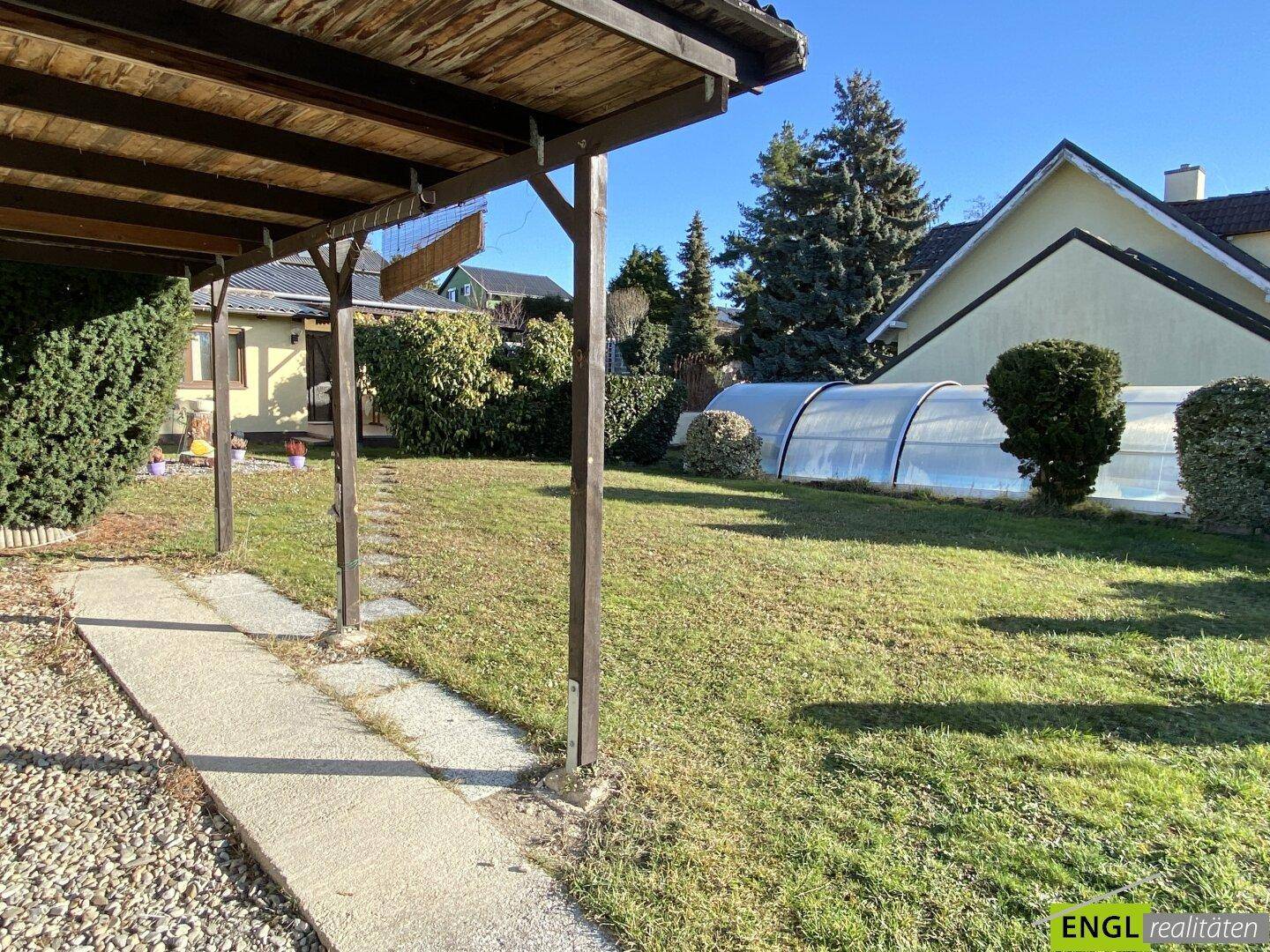 Gepflegter Gartenbereich mit Rasenfläche und einem überdachten Swimmingpool im Hintergrund.