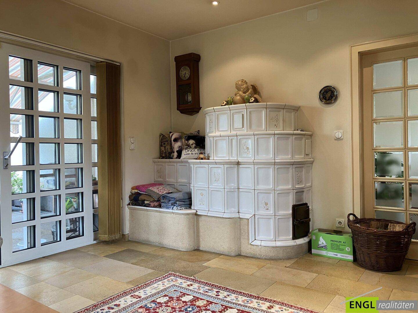 Heller Wohnbereich mit einem traditionellen Kachelofen und Zugang zum Garten.