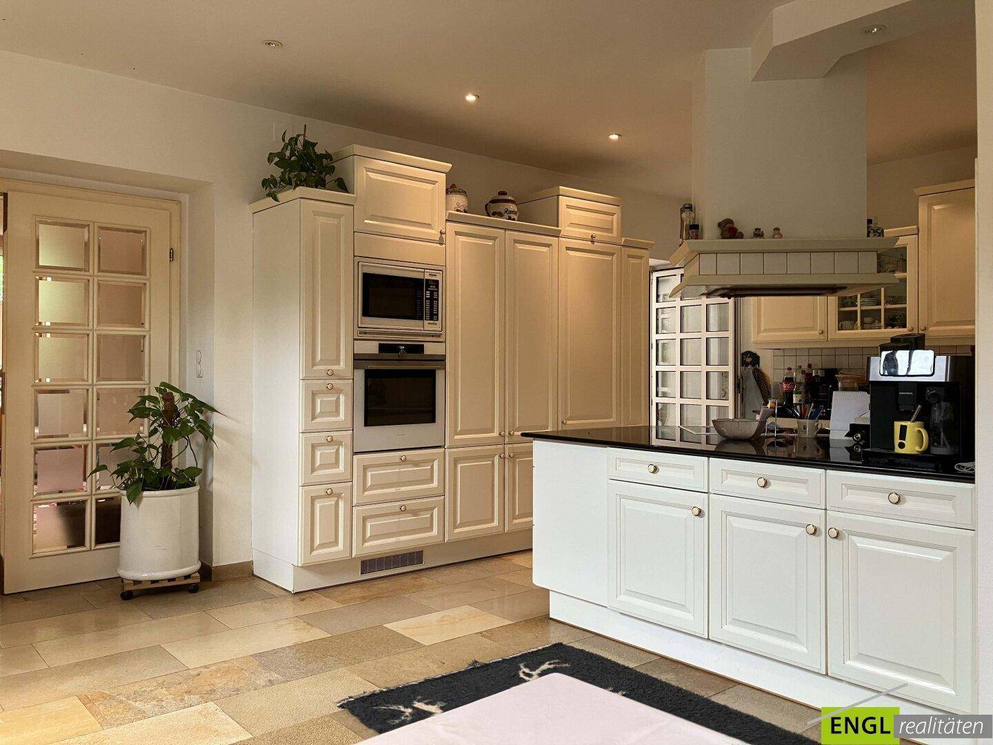 Geräumige, helle Küche mit weißen Einbauschränken, modernen Geräten und Fliesenboden.